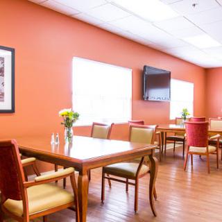 A cozy dining area with orange walls and comfortable seating, featuring natural light and a television.