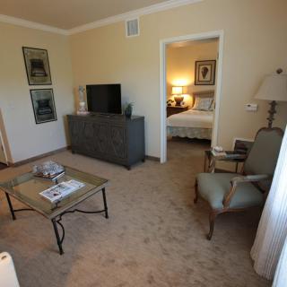 A cozy living room with a view into an adjoining bedroom, featuring a television, armchairs, and coffee table.