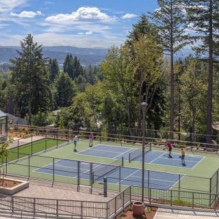 A scenic view of outdoor tennis courts surrounded by trees and hills in the background.