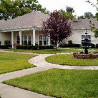 A charming house with a well-maintained lawn and a central pathway leading to the entrance, surrounded by lush greenery and a decorative fountain.