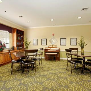 A cozy dining area with tables, chairs, and a piano against a decorated wall.
