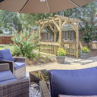 A cozy outdoor patio setup featuring comfortable seating and a wooden archway in a lush garden.