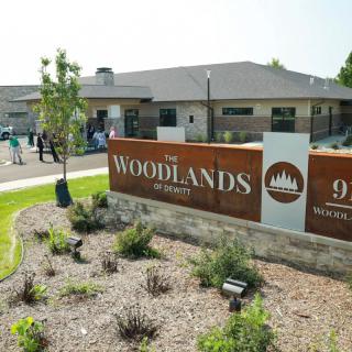 The entrance of Woodlands community center featuring a landscaped area and a prominent sign.