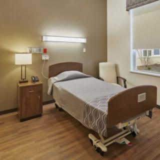 A neatly arranged hospital room with a single bed, chair, and bedside lamp.