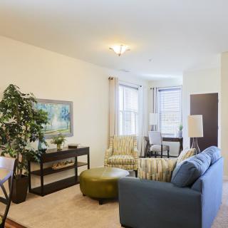 A cozy living room with a sofa, chairs, and a coffee table, decorated with plants and artwork.