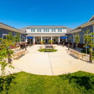 A sunny courtyard with benches and young trees, surrounded by a modern building.