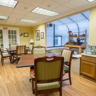 A cozy dining area with wooden chairs and tables, featuring bright lighting and a large window.