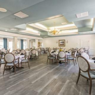An elegant dining room with neatly arranged tables and chairs, featuring a light blue ceiling and large windows.
