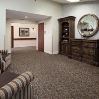 A cozy hallway with a carpeted floor, featuring a wooden cabinet and a round mirror on the wall.