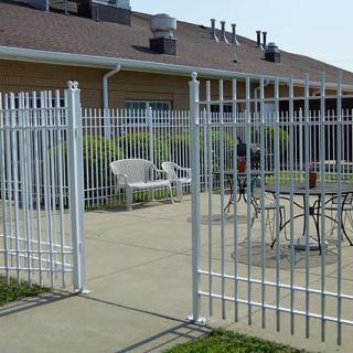 An outdoor patio area with a white fence and gate, featuring chairs and a table.