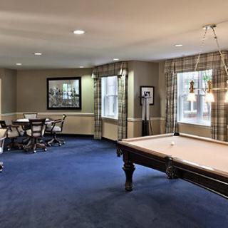 A stylish game room featuring a billiards table and a card-playing area with natural light streaming in through large windows.