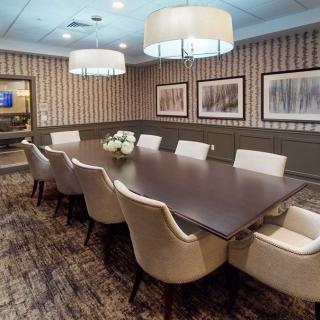 A well-appointed conference room with a long table, surrounded by chairs and illuminated by overhead lighting.