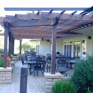 An outdoor patio area with a pergola, featuring tables and chairs for dining.