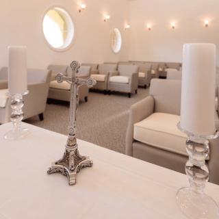 Interior of a chapel with a cross and candles on an altar, surrounded by seating.