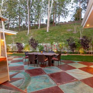 A cozy outdoor patio with a colorful checkered floor, surrounded by lush greenery and illuminated garden lights.