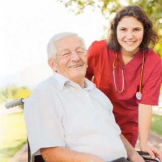 A smiling elderly man in a wheelchair with a nurse outdoors.