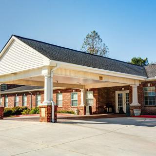 A building with a covered entrance and parking area on a clear day.