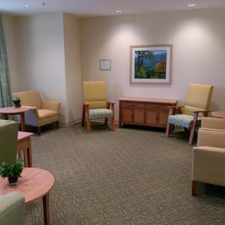 A quiet waiting room with several chairs, small tables, and a painting on the wall.