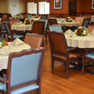 A warmly decorated dining room with neatly arranged tables and chairs, featuring floral centerpieces and folded napkins.