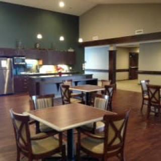 A cozy dining area with wooden tables and chairs, featuring a serving counter and ambient lighting.