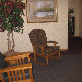 A cozy living room with a wooden rocking chair and a framed landscape painting on the wall.