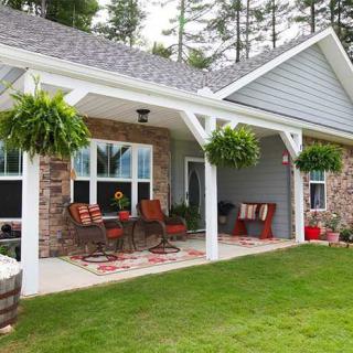 A cozy porch with comfortable seating and hanging plants, attached to a house with brick walls and a well-kept lawn.