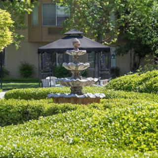 A tranquil garden featuring a beautiful fountain, surrounded by lush greenery and a gazebo.