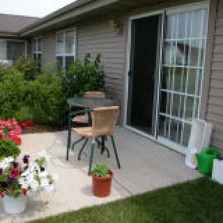 A cozy patio with a table and chairs, surrounded by plants and flowers.