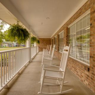 A peaceful suburban porch featuring white rocking chairs and hanging plants.