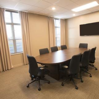 A modern conference room with a large table and chairs, featuring windows and a wall-mounted television.