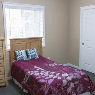A cozy bedroom with a single bed, a wooden dresser, and a window letting in natural light.