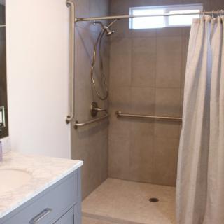 A bathroom featuring a tiled shower with grab bars and a curtain, adjacent to a sink.