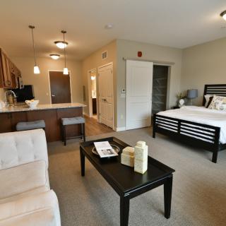 A modern studio apartment with an open layout, featuring a kitchen area, living space, and bedroom in neutral tones.