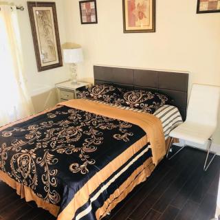 A neatly arranged bedroom featuring a stylish bed with patterned bedding, artwork on the walls, and a modern lamp on a side table.