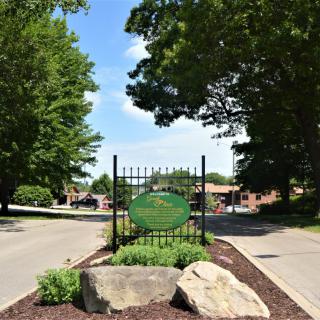 Entrance sign surrounded by trees and greenery on a sunny day.
