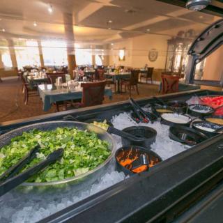 A salad bar in a spacious restaurant setting, featuring various fresh vegetables.