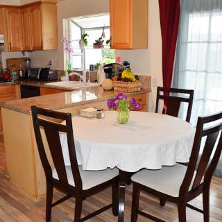 A cozy dining area with a round table covered by a white tablecloth, surrounded by wooden chairs, adjacent to a modern kitchen.