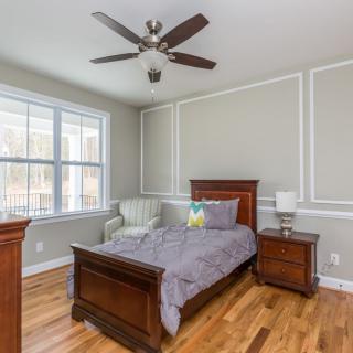 A cozy bedroom with a single wooden bed, hardwood floors, and a ceiling fan.