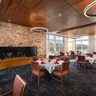 An elegant dining area with neatly set tables, a stone fireplace, and large windows providing natural light.