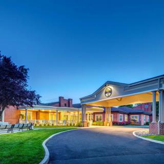 A well-lit hotel entrance during the evening, showcasing a landscaped exterior and clear sky.