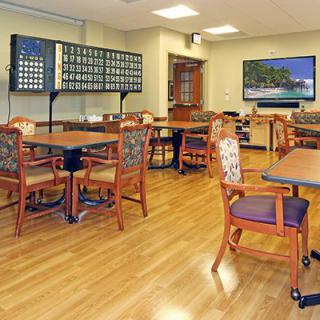 An empty bingo hall with wooden chairs and tables, featuring a large bingo board and a TV screen.