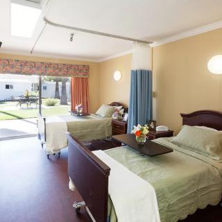 A well-lit hospital room with two patient beds and a view of an outdoor garden.