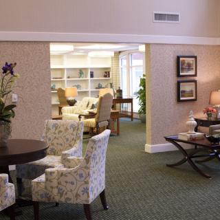 A cozy lounge area with floral chairs and a view into a small library.