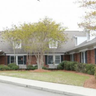 A brick residential building with manicured landscaping and trees at the front.