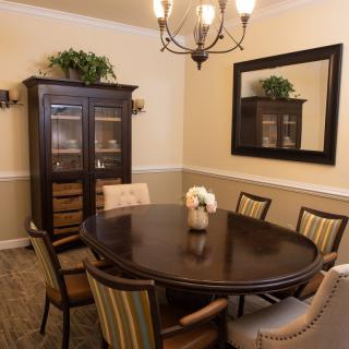 A cozy dining room with a round table, upholstered chairs, and a dark wooden cabinet.