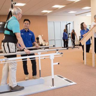 A patient receiving physical therapy assistance with the help of health professionals in a rehabilitation setting.