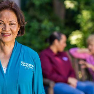 A caregiver smiling outdoors with elderly people in a nursing home setting.