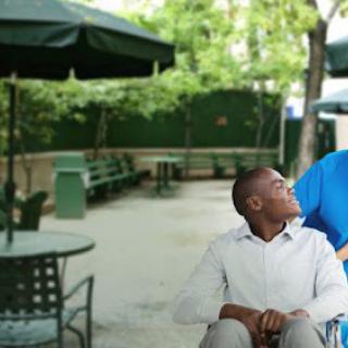 A person in a wheelchair having a conversation with another person outdoors.