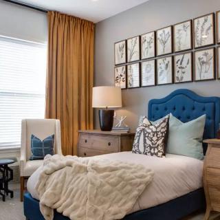 A modern bedroom with a blue tufted headboard, decorative wall art, and cozy furnishings.
