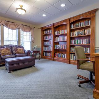 A cozy library with leather seating, wooden bookshelves, and a carpeted floor.
